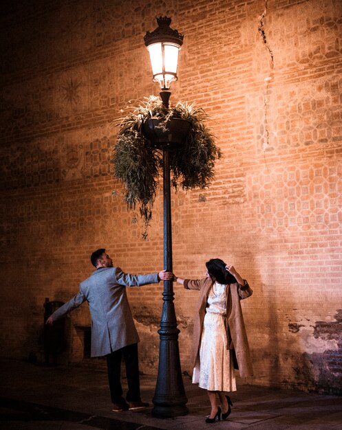 Elegante mujer y hombre joven girando cerca de farola iluminada