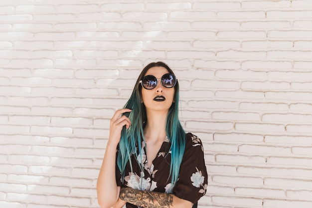 Elegante mujer joven con cabello teñido de pie frente a una pared beige