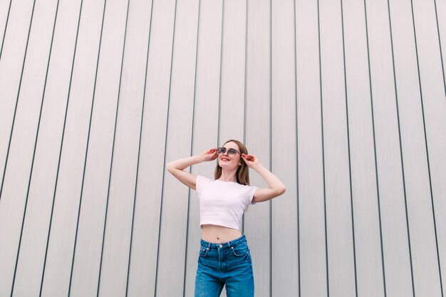 Elegante mujer joven camisa blanca posando en pared de rayas blancas