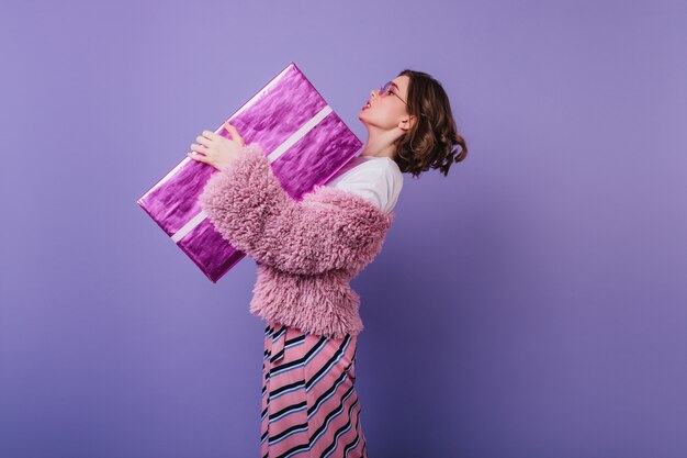 Elegante mujer joven en chaqueta de piel con gran regalo de cumpleaños. chica de pelo corto con caja de regalo rosa.