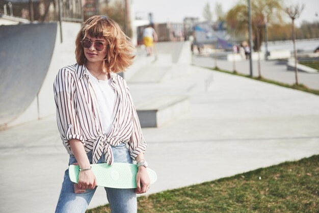 Elegante mujer joven hermosa con una patineta, en un hermoso día soleado de verano.