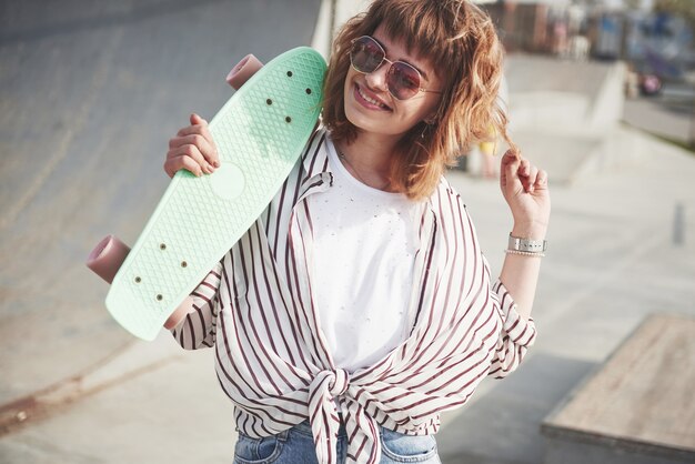 Elegante mujer joven hermosa con una patineta, en un hermoso día soleado de verano.