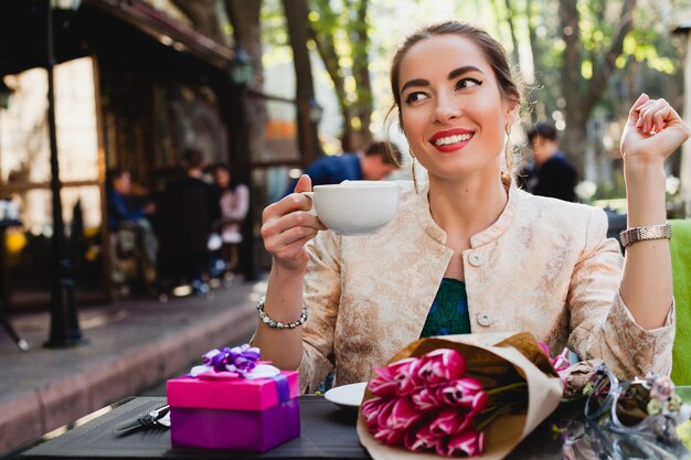 Elegante mujer joven sentada en la cafetería, sosteniendo una taza de capuchino