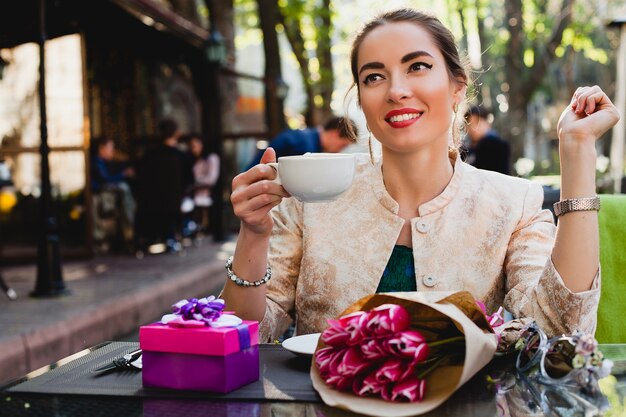 Elegante mujer joven sentada en la cafetería, sosteniendo una taza de capuchino