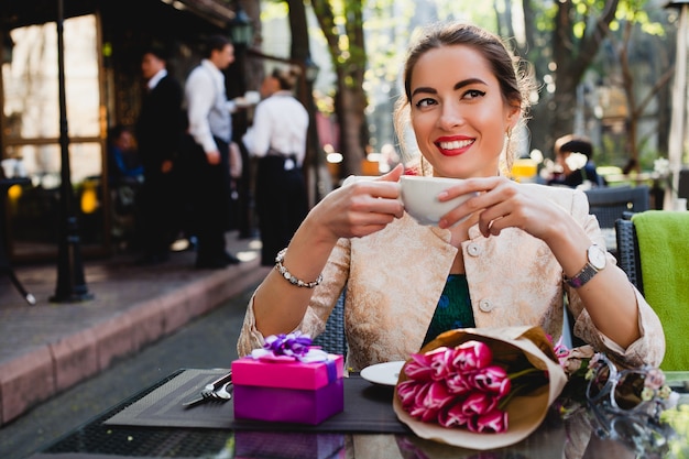 Elegante mujer joven sentada en la cafetería, sosteniendo una taza de capuchino