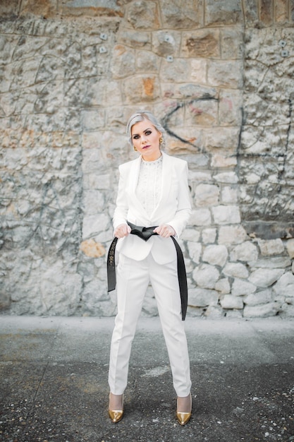 Elegante mujer de moda con un traje blanco con cinturón negro y pantalones posando para una sesión de fotos de moda