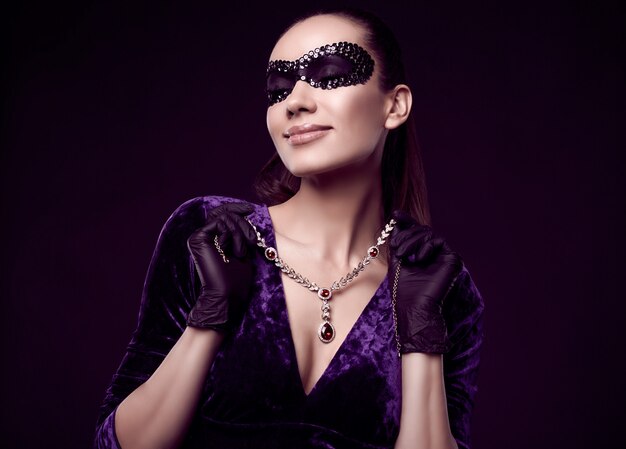 Elegante mujer morena con hermoso vestido morado, máscara de lentejuelas y guantes negros