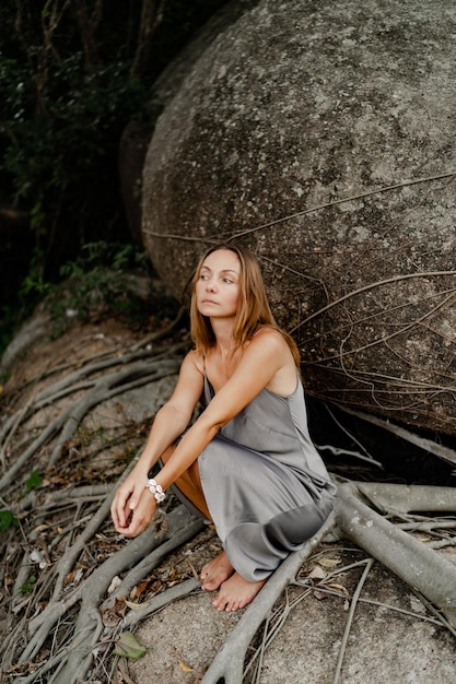 Elegante mujer morena con vestido gris de seda posando en las rocas