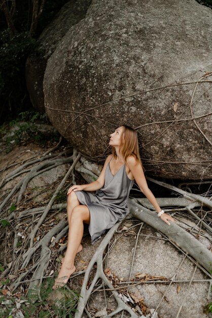 Elegante mujer morena con vestido gris de seda posando en las rocas