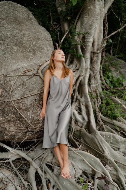 Elegante mujer morena con vestido gris de seda posando en las rocas