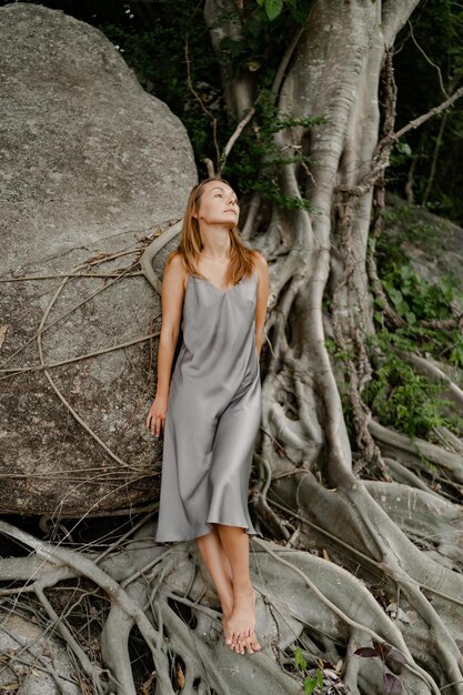 Elegante mujer morena con vestido gris de seda posando en las rocas