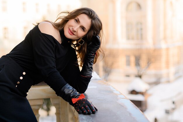 Elegante mujer de negocios caucásica adulta posando en el balcón Mujer elegante con ropa y guantes negros de moda Persona atractiva Rostro de belleza