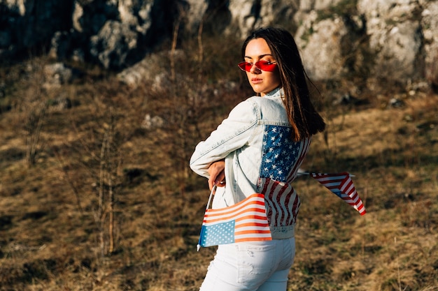 Foto gratuita elegante mujer de pie en la naturaleza con banderas de estados unidos