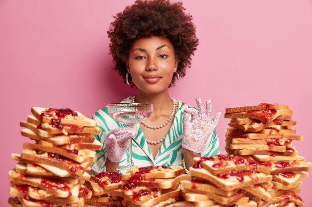 Elegante mujer retro se degusta, hace un signo perfecto, vestida con un vestido elegante con joyas y guantes de encaje, en una fiesta nocturna en un restaurante de lujo, tiene la tentación de comer deliciosas tostadas.