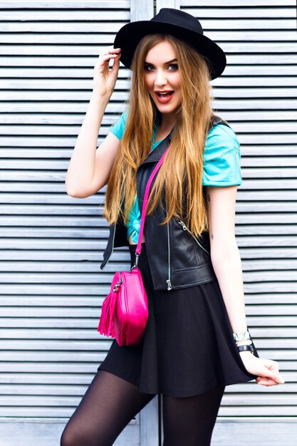 Elegante mujer rubia posando en la calle, vestida con traje brillante hipster, divertidas emociones frescas, diversión, disfrute, felices vacaciones solo, sombrero vintage y minifalda.