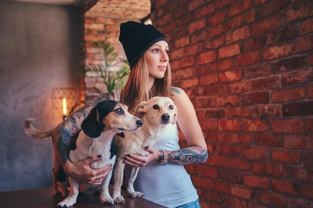 Una elegante mujer rubia tatuada con camiseta y jeans abraza a dos lindos perros.