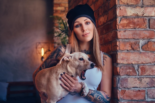 Foto gratuita una elegante mujer rubia tatuada con camiseta y jeans sostiene un lindo perro.