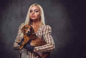 Foto gratuita una elegante mujer rubia vestida con una chaqueta antigua sostiene un perro tejón rojo.