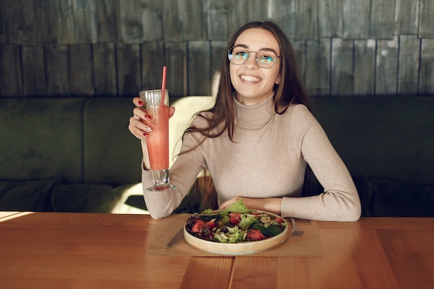 Elegante mujer sentada en la mesa con cóctel y ensalada