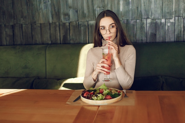 Foto gratuita elegante mujer sentada en la mesa con cóctel y ensalada