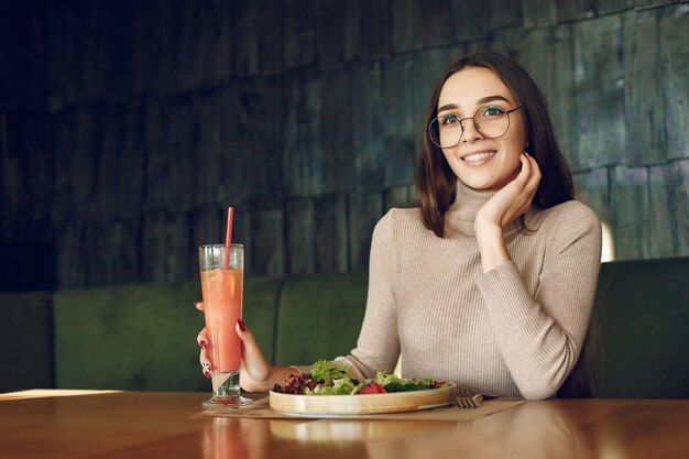 Elegante mujer sentada en la mesa con cóctel y ensalada