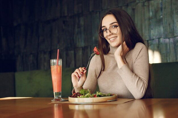 Elegante mujer sentada en la mesa con cóctel y ensalada