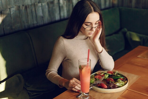 Elegante mujer sentada en la mesa con cóctel y ensalada