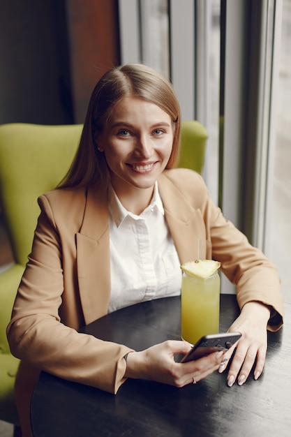 Elegante mujer sentada en la mesa con cóctel y teléfono