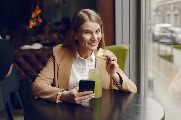 Elegante mujer sentada en la mesa con cóctel y teléfono