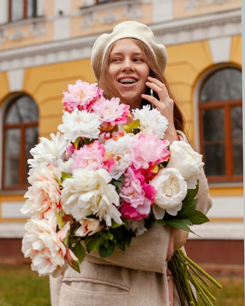 Elegante mujer sonriente sosteniendo un ramo de flores al aire libre en la primavera y hablando por teléfono