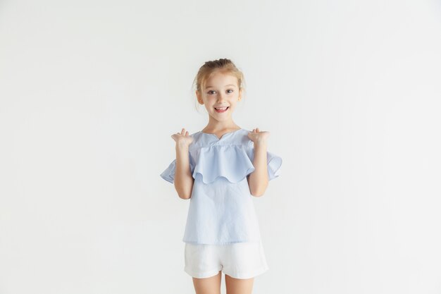 Elegante niña sonriente posando en ropa casual aislado sobre fondo blanco de estudio. Modelo de mujer rubia caucásica. Emociones humanas, expresión facial, infancia. Mostrar, invitar o saludar.