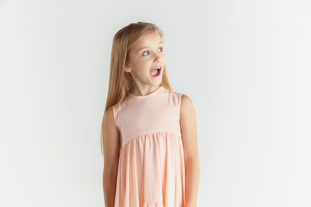 Elegante niña sonriente posando en vestido aislado sobre fondo blanco de estudio. Modelo de mujer caucásica. Las emociones humanas, la expresión facial, la infancia. Asombrado, asombrado, conmocionado. Mirando de lado.