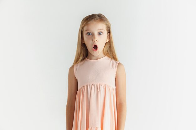 Elegante niña sonriente posando en vestido aislado sobre fondo blanco de estudio. Modelo de mujer rubia caucásica. Las emociones humanas, la expresión facial, la infancia. Asombrado, asombrado, conmocionado.