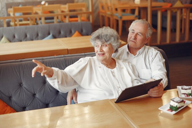 Elegante pareja de ancianos en un café con una tableta