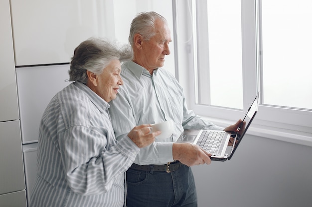 Elegante pareja de ancianos en casa usando una computadora portátil