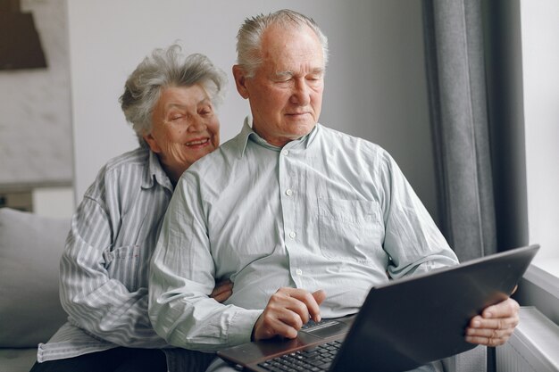 Elegante pareja de ancianos sentados en casa y usando una computadora portátil