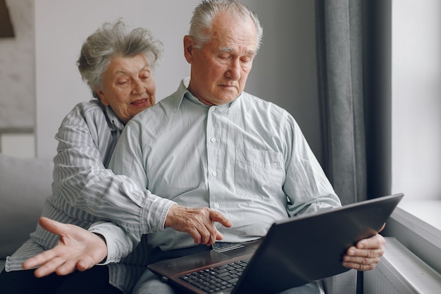 Elegante pareja de ancianos sentados en casa y usando una computadora portátil