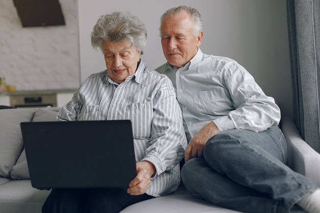 Elegante pareja de ancianos sentados en casa y usando una computadora portátil