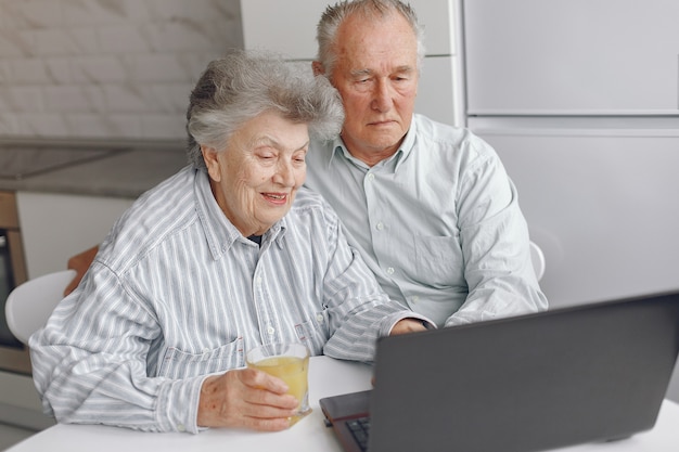 Elegante pareja de ancianos sentados en casa y usando una computadora portátil