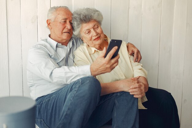 Elegante pareja de ancianos sentados en casa y usando un teléfono