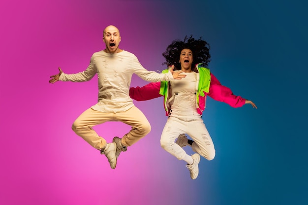 Foto gratuita elegante pareja caucásica deportiva bailando hiphop sobre un colorido fondo degradado en el salón de baile con luz de neón