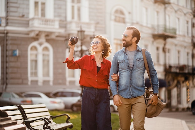 Elegante pareja de enamorados caminando abrazándose en la calle en un viaje romántico y tomando fotos