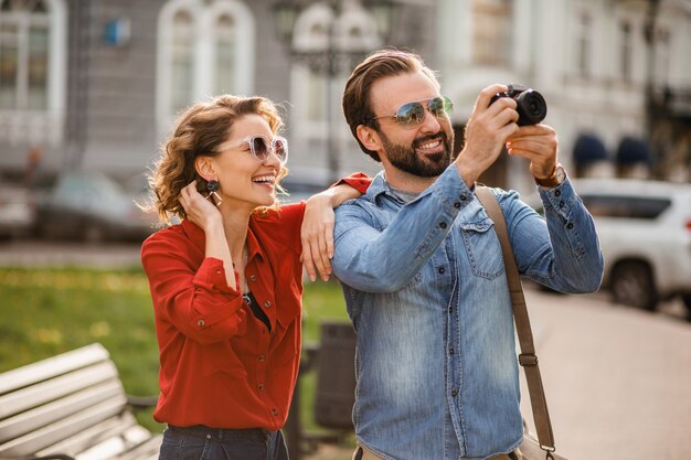 Elegante pareja de enamorados caminando abrazándose en la calle en un viaje romántico y tomando fotos