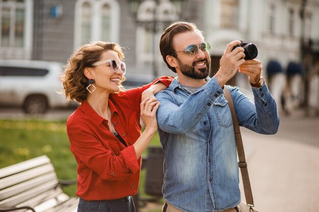 Elegante pareja de enamorados caminando abrazándose en la calle en un viaje romántico y tomando fotos