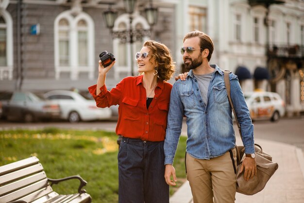 Elegante pareja de enamorados caminando abrazándose en la calle en un viaje romántico y tomando fotos