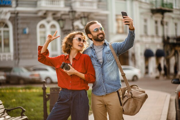 Elegante pareja de enamorados caminando abrazándose en la calle en un viaje romántico y tomando fotos