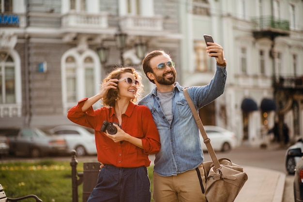 Elegante pareja de enamorados caminando abrazándose en la calle en un viaje romántico y tomando fotos