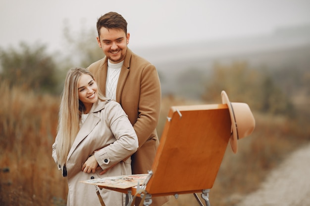 Elegante pareja pintando en un campo de otoño