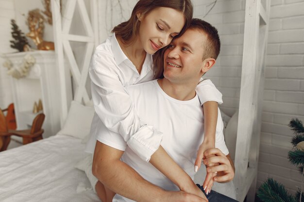 Elegante pareja sentada en una cama cerca del árbol de navidad