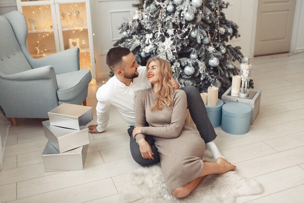 Elegante pareja sentada en casa cerca del árbol de navidad